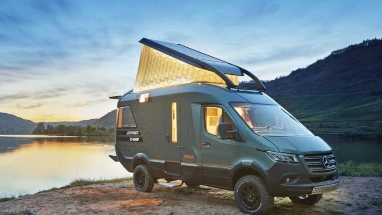 The Hymer VisionVenture campervan stands by a lake at dusk with the folding roof open.