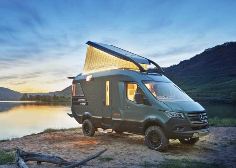 The Hymer VisionVenture campervan stands by a lake at dusk with the folding roof open.